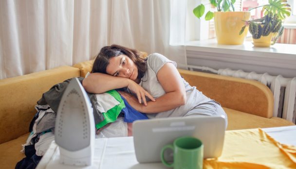 Tired,Middle,Aged,Woman,Watches,Video,On,Tablet,And,Ironing